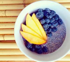 maple cardomom chia pudding white bowl with maple cardamom chia pudding, fresh blueberries and mango on top of a bamboo background